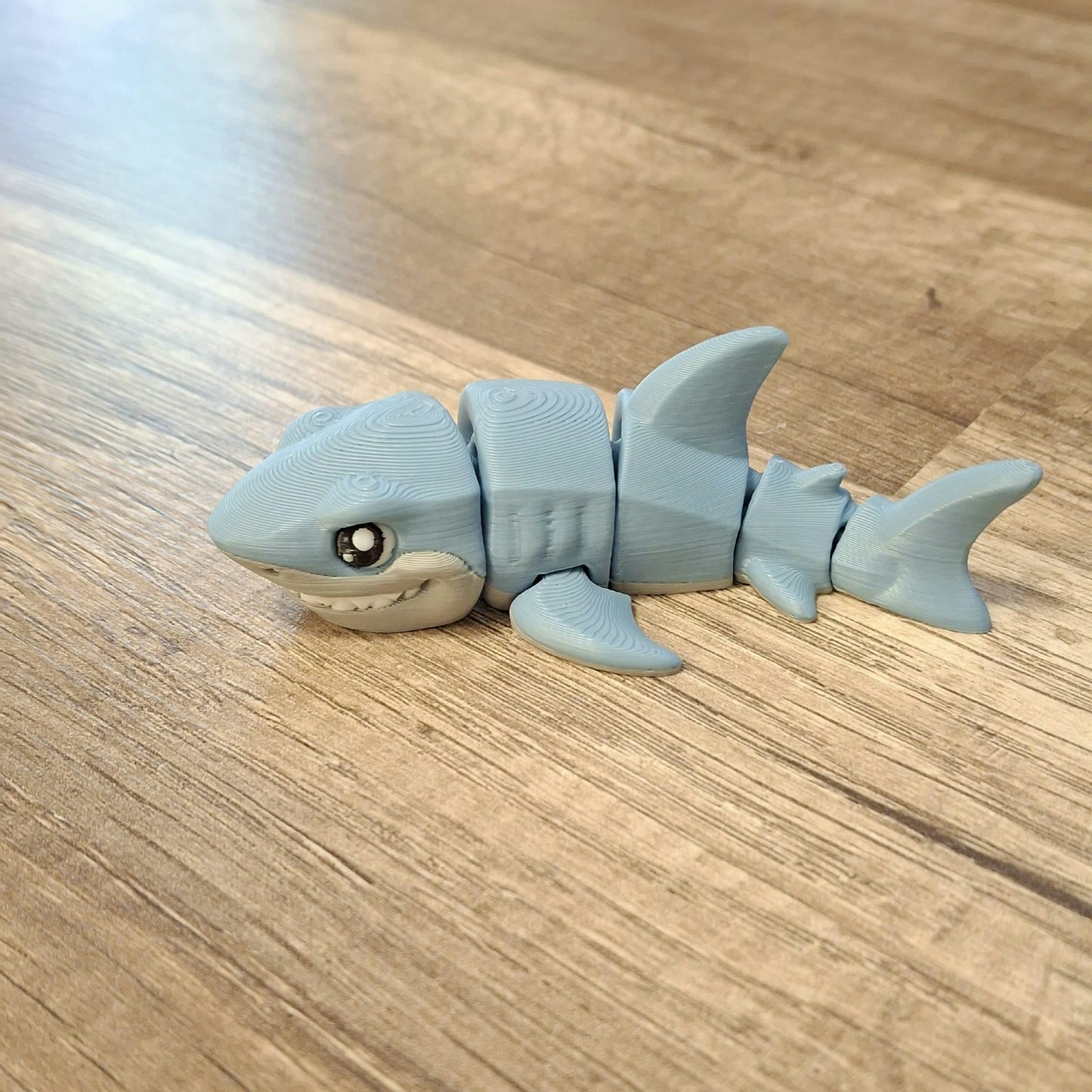 “3D printed articulated great white shark toy with moving fins and body segments displayed on a wooden surface.”