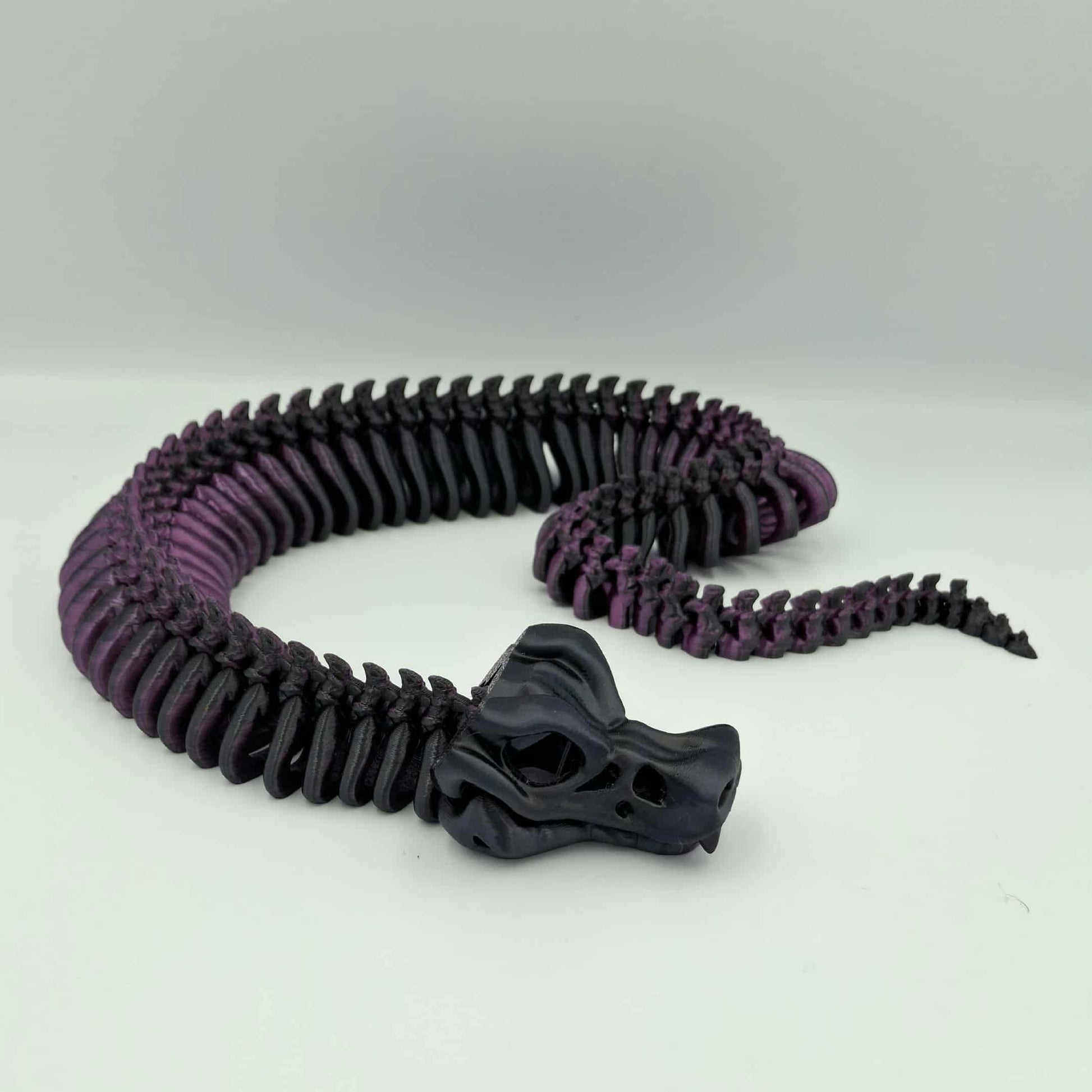 3D printed articulated skeleton snake in black and red gradient with poseable body and an opening jaw.