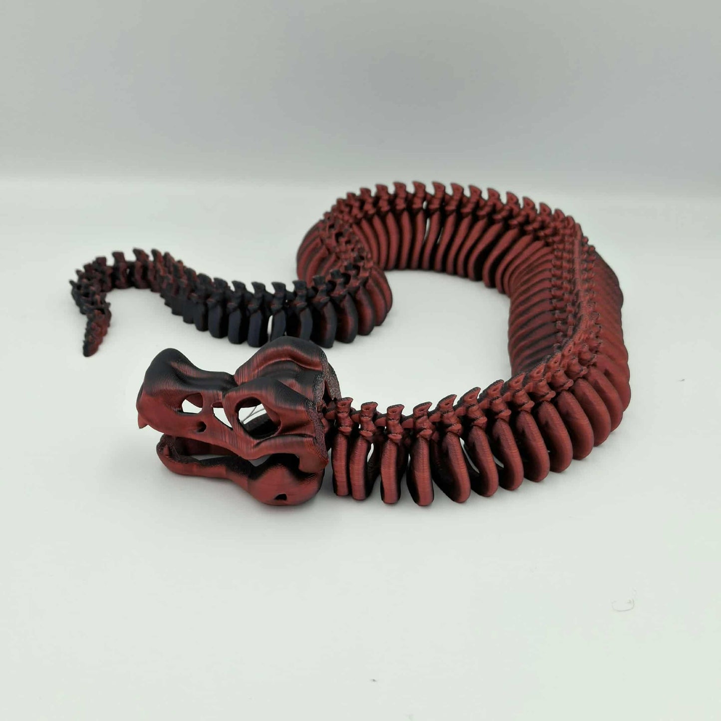 3D printed articulated skeleton snake in black and red gradient with poseable body and an opening jaw.