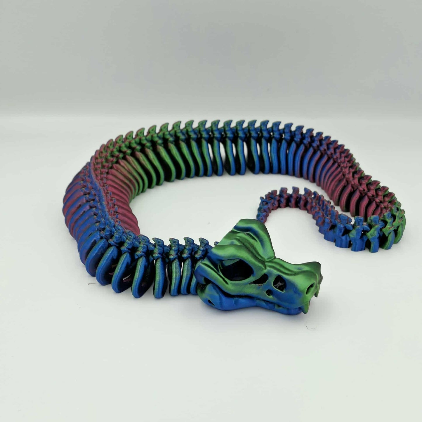 3D printed articulated skeleton snake in black and red gradient with poseable body and an opening jaw.